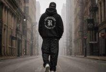 Flat-lay of a black stussy hoodie, white Amiri MA-1 sneakers, and a graphic mixed emotions shirt on a concrete floor.