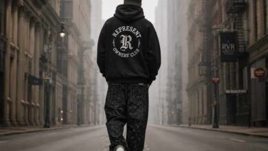 Flat-lay of a black stussy hoodie, white Amiri MA-1 sneakers, and a graphic mixed emotions shirt on a concrete floor.
